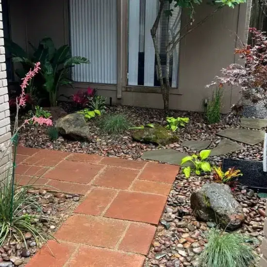 Landscape maintenance in Houston featuring a front courtyard with a blend of tropical and botanical plants, enhanced by decorative river stone and ornamental rock for a natural, elegant look.