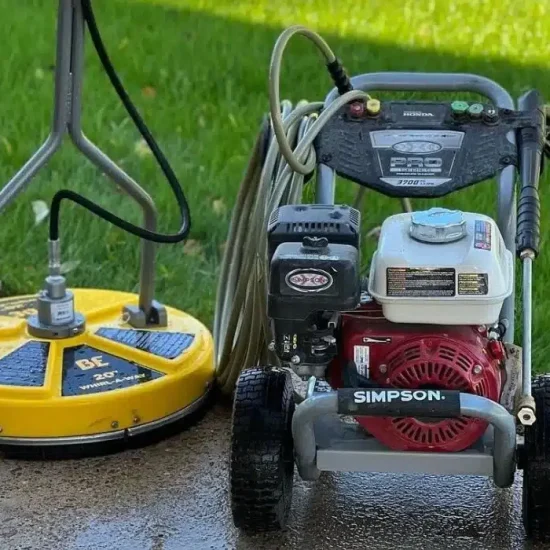 Professional-grade equipment used for pressure washing service, positioned on a wet concrete walkway with a freshly cleaned lawn in the background.